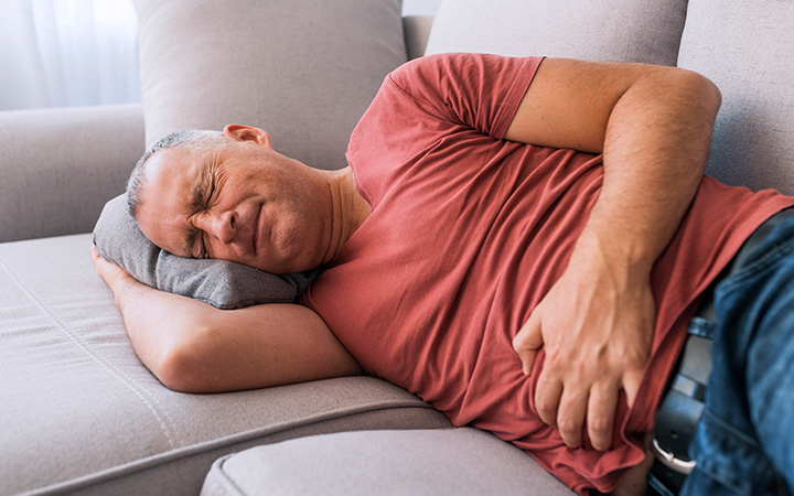 Man lying on couch clutching stomach