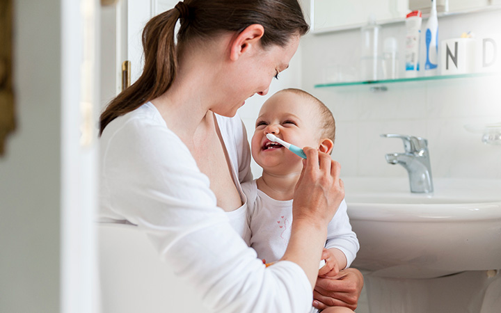 young mom holding baby and putting toothbrush in baby's mouth