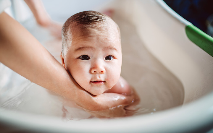 small baby in bathtub held by adult arms